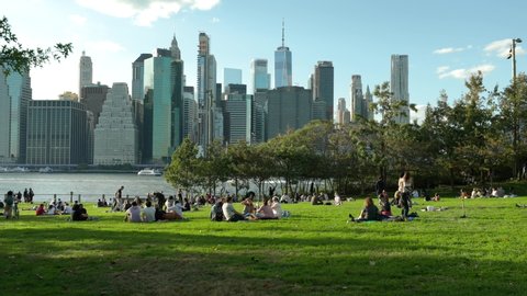 New York, NY / USA - October 10 2020: People sitting on the green grass of the Brooklyn Bridge Park with the Manhattan Skyline on the background 
