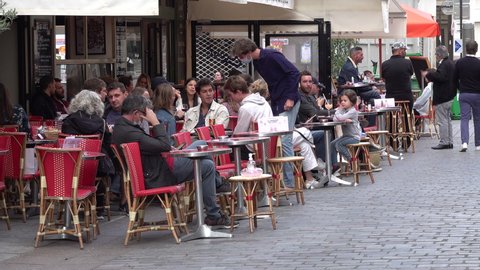 PARIS, FRANCE – SEPTEMBER 2020: People enjoy drinks, snacks, and dinner at busy outdoor terrace of restaurant in Paris, France. Waiters are wearing face masks, Covid-19 coronavirus regulation