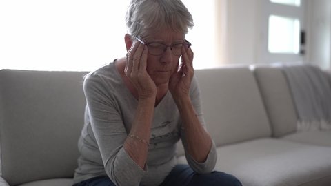 Unhappy headache Retired Senior Woman Sitting On Sofa At Home