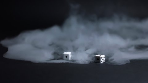 Throwing white dice across some low laying fog on a black background in slow motion.