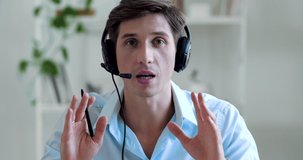 Serious male teacher wears headphones speaks in microphone communicates in video chat, shares information knowledge in camera. Portrait of call manager working on help line advising clients online