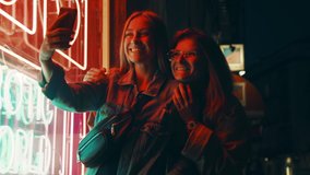 Happy flirting friends, send love and kisses to followers on social media. Two young women pose for selfie photos or video on smartphone camera. Night time screen lit image in neon lights - Powered by Shutterstock - Get 15% off with code: PIKWIZARD15