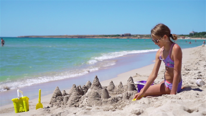 Little adorable girl at tropical beach making sand castle