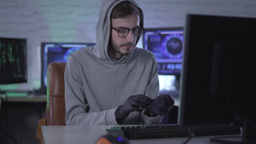 Purposeful man in eyeglasses putting on black gloves and typing on computer keyboard. Portrait of male Caucasian hacker stealing information from office or hacking security password. Royalty-Free Stock Footage #1061281174