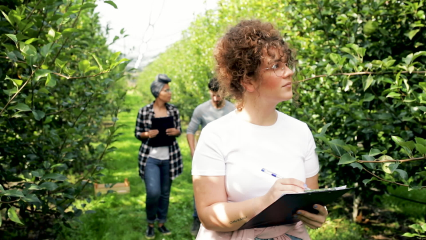 Portrait if young female farmer examining quality of pears in orchard.