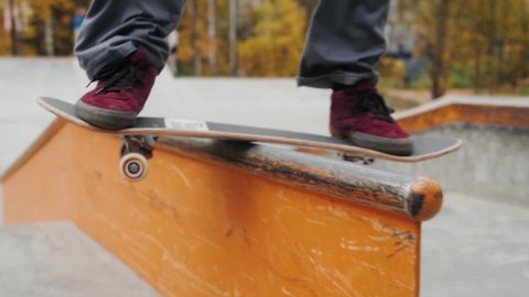 Skater practicing in the autumn concrete skate park, making tricks and rides in ramp. Skateboarder making tricks, manual balance, boardslide and stalls, professional extreme sport