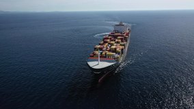 Aerial drone video of container ship with colourful truck size containers cruising in open ocean Mediterranean Aegean sea, Greece