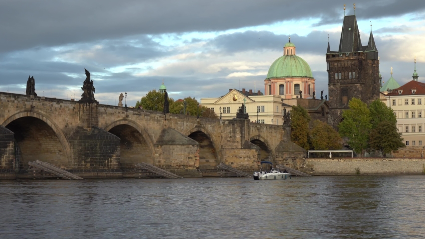 shot in the motion of the Charles Bridge from the 14th century and the Vltava river in the center of Prague. The sky is blue with clouds and buildings illuminated by the sun