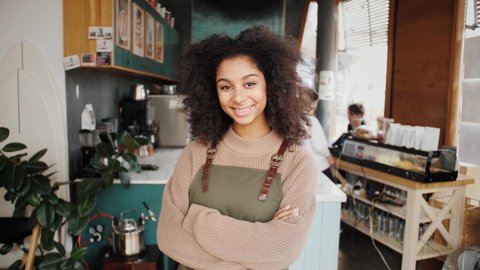 Happy stylish African American woman, generation z female with Afro hair looks at camera stands in cafe interior. Smiling mixed race latin young woman headshot portrait. Work for international