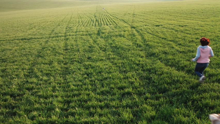 Woman with dog running to little girl across green field