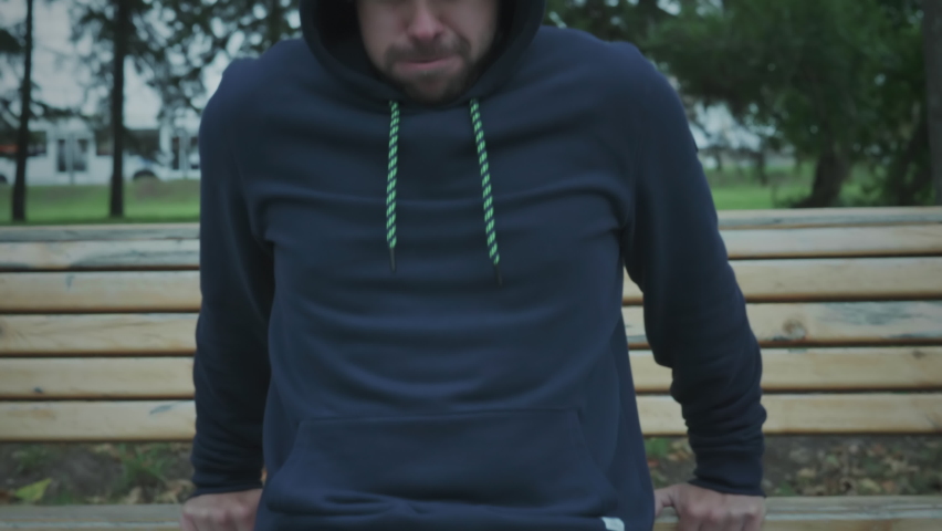 Close-up of young man athlete wearing hoodie engaged in push up exercises with exhausted facial expression. Man making push up work out