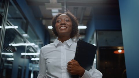 Smiling african business woman saying hi in office corridor. African american businesswoman greeting employee in corridor. Closeup beautiful afro woman waving hand in business center hallway