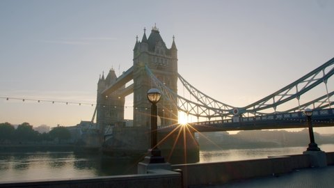 Lockdown in London, two birds swoop in front of stunning slow motion gimbal pan of a sunrise sun flare through Tower Bridge at golden hour, during 2020's COVID-19 pandemic.