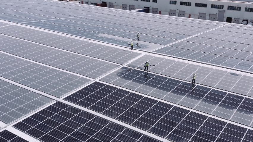 Men At Work On The Roof Of A Warehouse Cleaning Solar Panels - ascending drone shot Royalty-Free Stock Footage #1061297794
