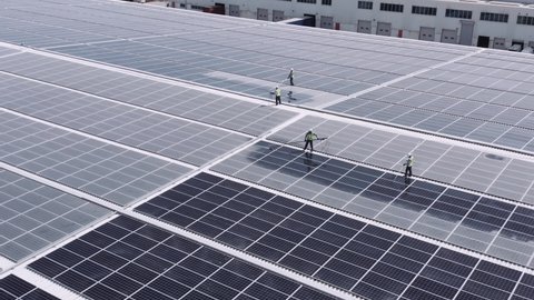 Men At Work On The Roof Of A Warehouse Cleaning Solar Panels - ascending drone shot