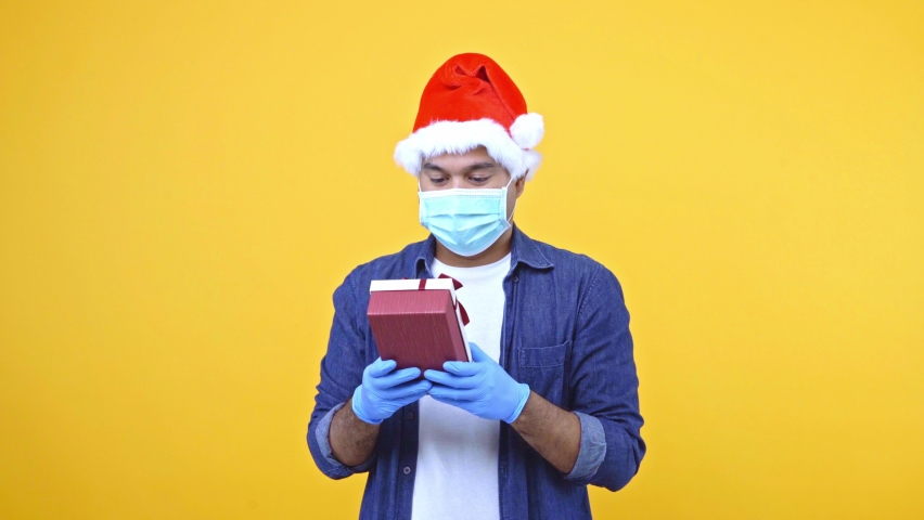 Funny guy secretly open the gift box. He lookin what inside the box. He wearing protection mask and medical rubber gloves safety form coronavirus. Christmas eve festival concept. 4K Resolution.