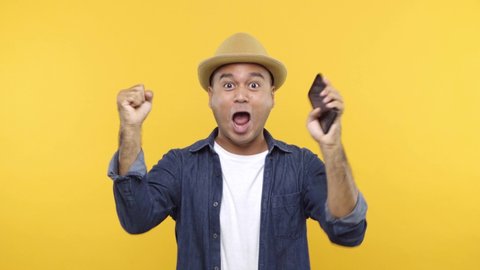 Asian man in denim jacket white t-shirt look to smartphone posing doing winner gesture, say Yes isolated on yellow background. 4k Resolution.