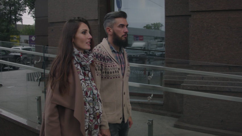 Middle-aged man and woman walking in love through the city streets in autumn on a cloudy day. A man in a sweater and a woman in a coat are walking around the city together.