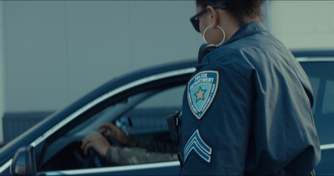 African-American black driver is being pulled off by mixed-race female police officer. Documents check, speeding ticket. Shot on RED cinema camera with 2x Anamorphic lens