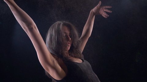 a young energetic woman in a black suit in a Studio on a black background dancing, moving and posing. It's covered in sand.