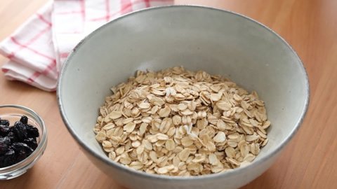 Oat flakes, rolled oats falling in a bowl. Preparation of oatmeal porridge. Healthy vegan vegetarian diet food ingredient
