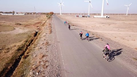 Cyclists ride along the road with a view of the windmills. Alternative, clean energy is produced. Ride on ecological transport. Travel on the road by Bicycle. Steppe. Top view from a drone. Kazakhstan