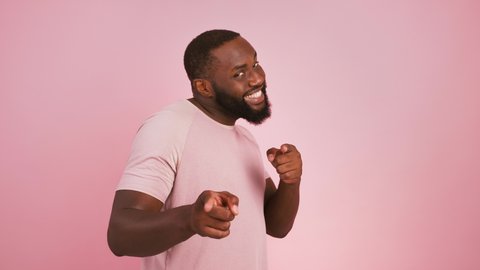 Hey you! Profile portrait of black man turning to camera and indicating happily at camera, choosing and smiling, pink studio background
