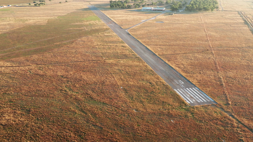 Empty runway of a small airport used for takeoff and landing of light aircraft. Airfield for general aviation and light-sport planes in the middle of a field covered with yellow grass. Royalty-Free Stock Footage #1061311438