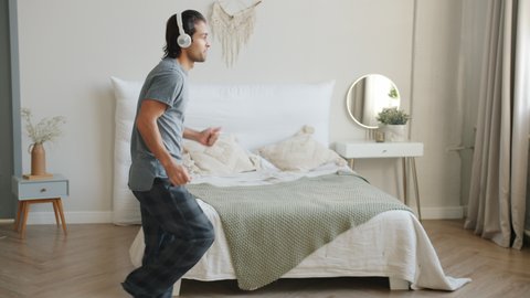 Handsome young man is dancing at home in bedroom enjoying music in headphones having fun indoors in leisure time. Youth and entertainment concept.