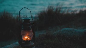 Old classic oil lantern burning with an orange flame by the ocean at dusk. Blurred background. - Powered by Shutterstock - Get 15% off with code: PIKWIZARD15