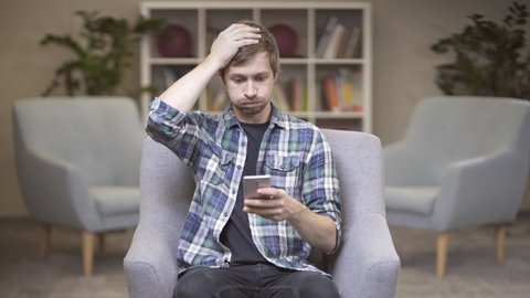Portrait of young man looking confused over the news he received on his smart phone, the man showing a disappointed gesture