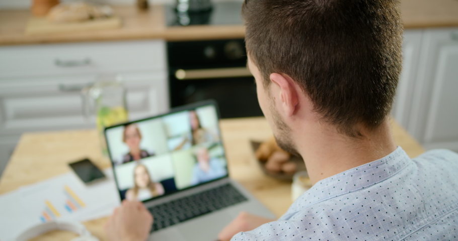Man in Headphones Talks with 4 People at Video Chat using Laptop in Kitchen. Online Group Video Call Conference of Work Team from Home Office. Self-isolation at COVID-19 Pandemic. 4K Medium Shot Royalty-Free Stock Footage #1061317582