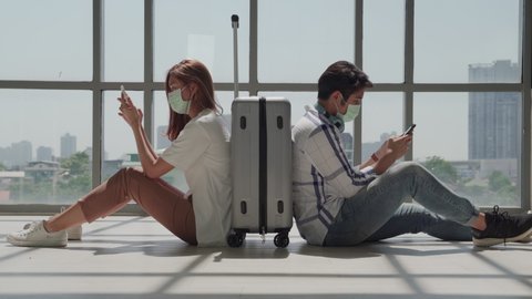 In the midst of the COVID-19 outbreak, a masked couple sitting on their cell phone relieves boredom from a postponed flight.