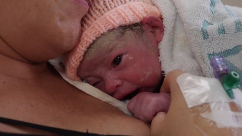4K: Newborn baby laying on her Mum in hospital bed / Maternity ward. The child has a hat on and is close by her mother. Stock Video Clip Footage