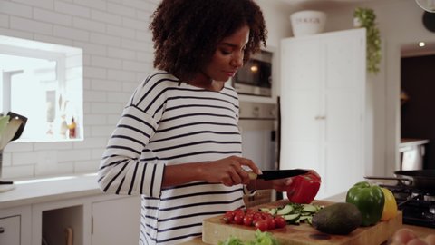 Zoom out shot of a young african woman cutting fresh colorful vegetables with knife foe preparing healthy salad in kitchen 库存视频
