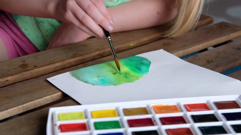 Child draws with watercolors on a sheet of paper, close-up