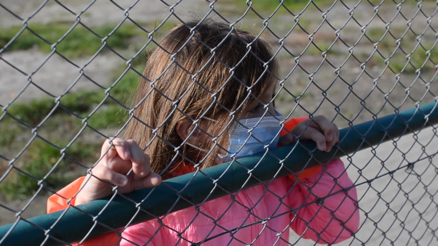 Little girl child in medical mask behind an iron fence