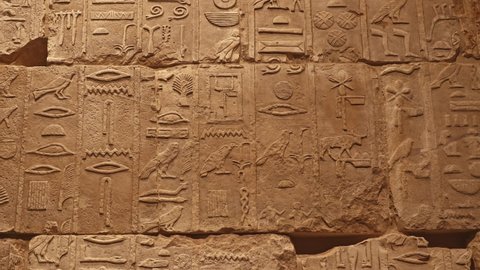 Background of antique stone wall with carved ancient Egyptian hieroglyphs, close up, pan front view