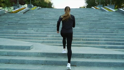 Fit woman wearing black sportswear and white sports shoes running upstairs in city park. Following shot female jogger training in the morning. Concept of fitness
