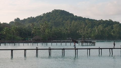 7 oct 20, Koh Kut Island, Thailand. workers walking on wooden bridge over the sea near tropical beach resort. sunrise in the morning with beam on mountain.