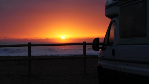 Camper vehicle camping on beach seashore at sunrise. Sea waves moving in slow motion. Spain, Costa Blanca, Alicante province.