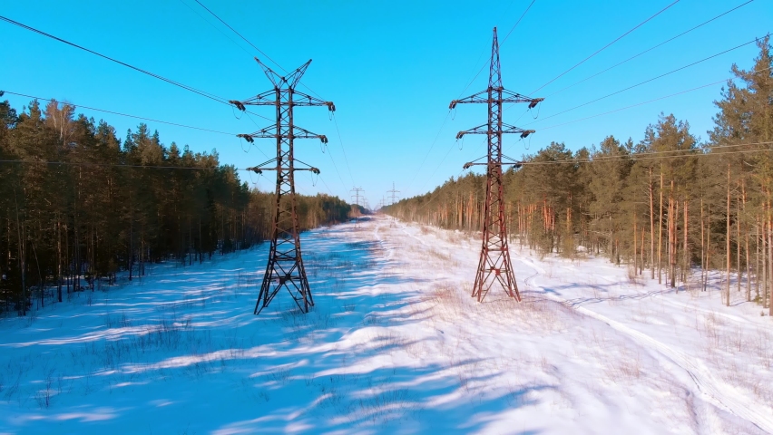 Aerial view from a drone. High voltage electrical line in the winter forest on a sunny day. Stock footage 4k