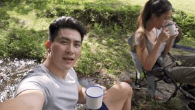 Asian couple camping at forest using smartphone with internet for video call or Vlogging. Happy man and woman friend enjoy and having fun with outdoor lifestyle together. Technology and people concept