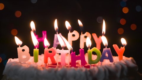 Dancing Candle Lights on the Cake. Cake with candles in the form of an inscription Happy Birthday. In the background, flashing and moving lights bokeh in the dark