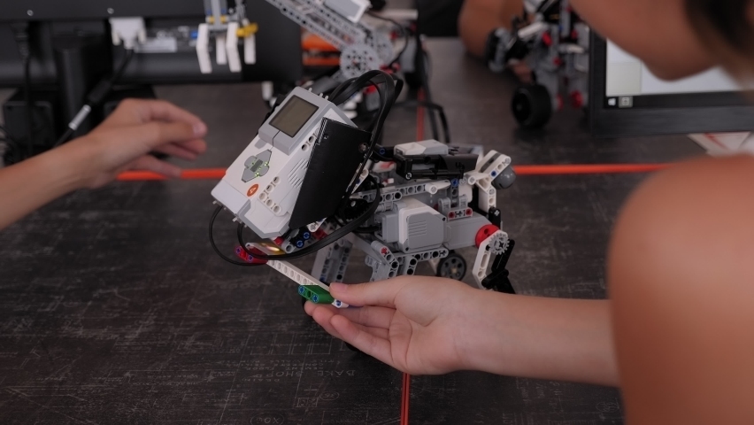Close-up of a group of children assembling a robot dog and an excavator from plastic parts programmed on a computer at a robotics school.