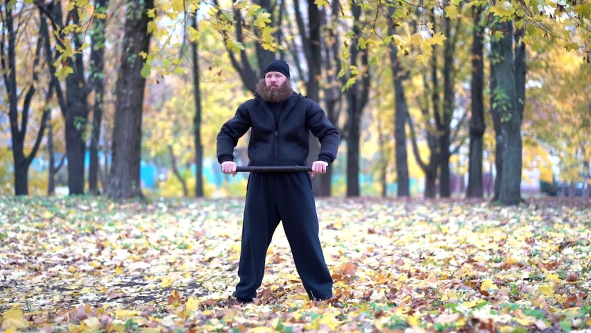 Dumbbell man. The guy in the black jacket and gray pants. Athlete doing gymnastics in the park. Gymnastic exercises outdoors in autumn. Lumberjack. Bearded man.