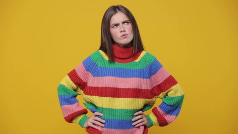 Puzzled excited young woman 20s years old in colorful rainbow sweater posing isolated on yellow background studio. People lifestyle concept. Put hand on head hold index finger up with great new idea