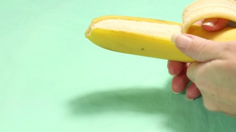Women's hands peel a ripe banana. Close-up on a turquoise background.