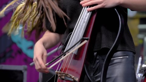 Slow motion: woman hands playing electric cello on stage of summer open air concert - close up view. Entertainment, music, culture, leisure time and art concept