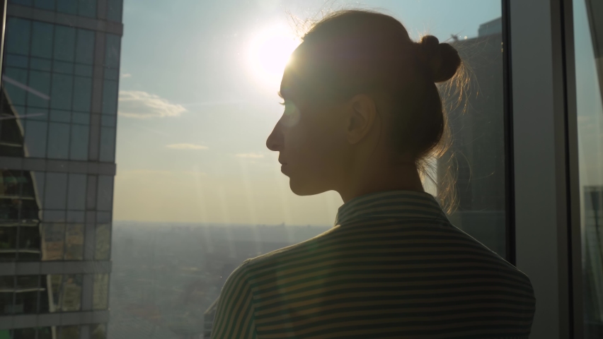 Success, opportunity, sightseeing, discover and future concept. Back view of pensive woman silhouette looking at cityscape through window of skyscraper. Summer time, sun lens flare, daylight Royalty-Free Stock Footage #1061344615